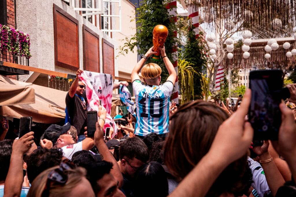 Argentina fan in a Messi number 10 jersey lifts a World Cup trophy replica above a celebrating crowd on a street