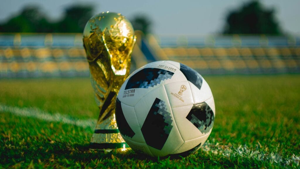 FIFA World Cup trophy and official match ball on a grass pitch inside a stadium