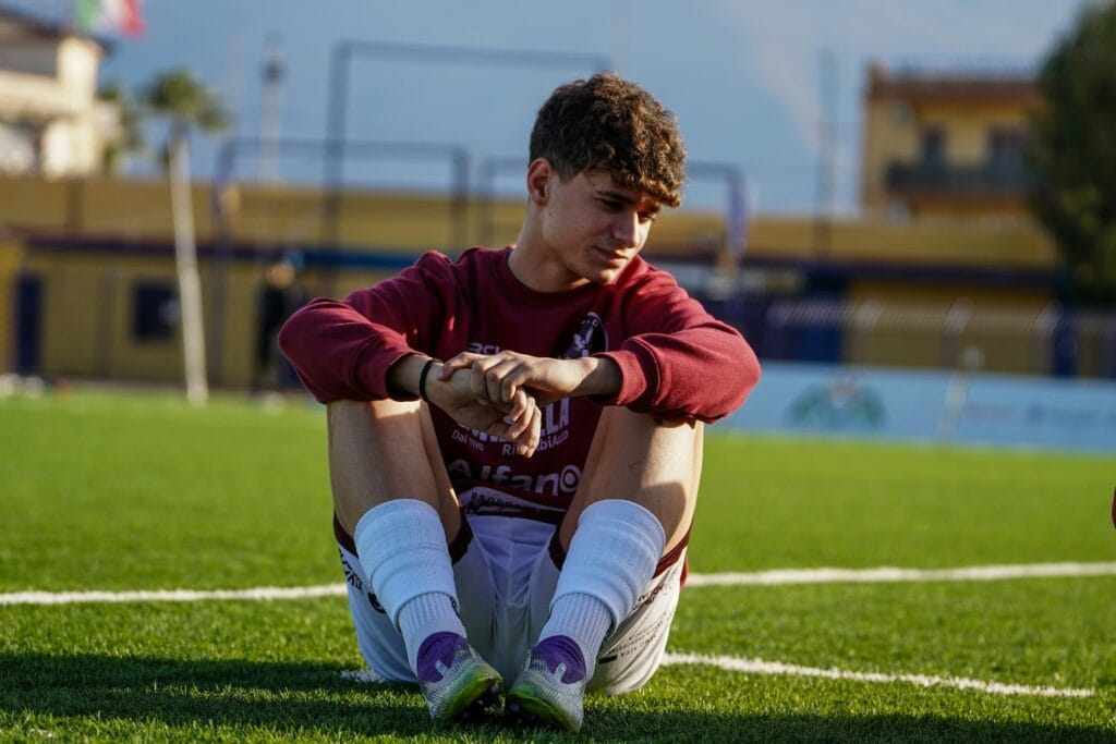 Young soccer player in a maroon kit sitting alone on the pitch, looking down, positioned near the article's discussion of the Adams-McKennie midfield pivot