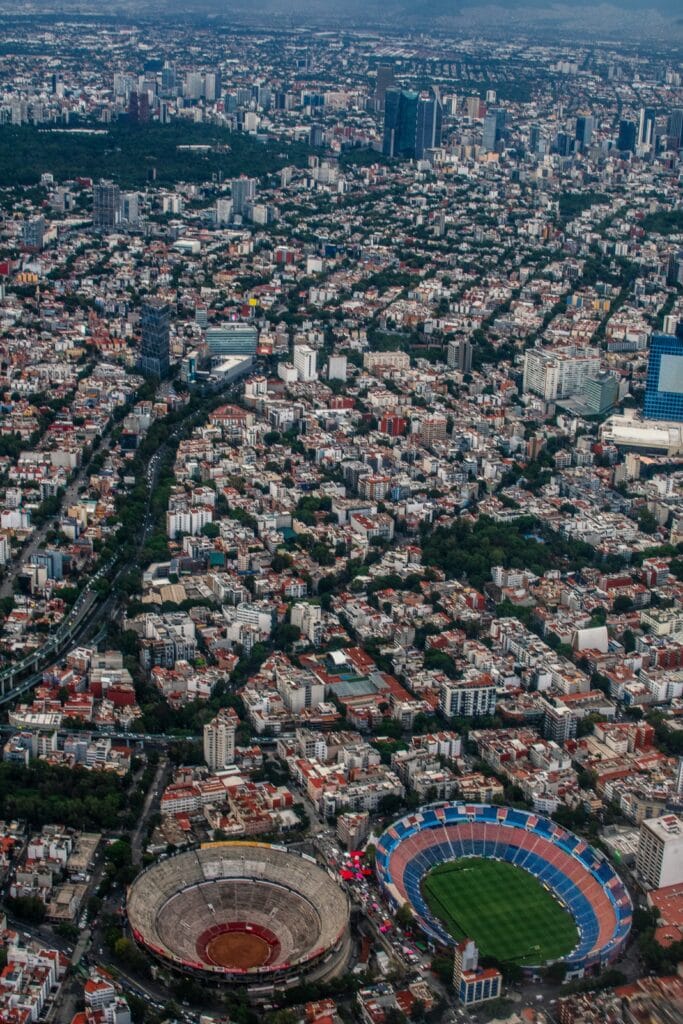 Aerial view of Mexico City's dense urban landscape with a bullring and a soccer stadium visible in the foreground