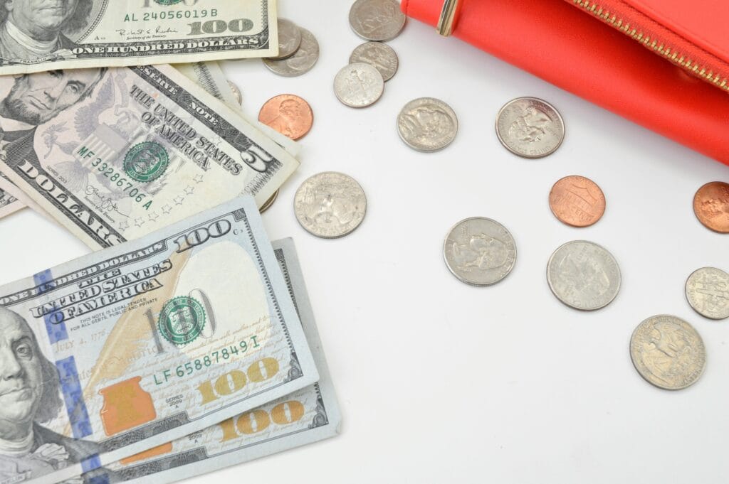 US dollar bills, loose coins, and a red wallet spread on a white surface, representing personal borrowing and money management