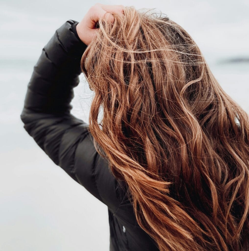 Woman running her hand through long wavy hair, illustrating scalp access and hair health
