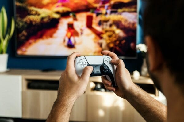 Person holding a PlayStation 5 DualSense controller while playing a colorful video game on a TV
