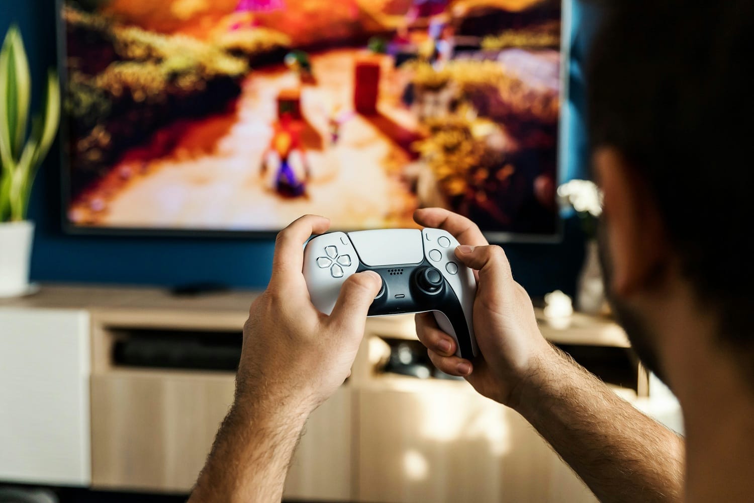 Person holding a PlayStation 5 DualSense controller while playing a colorful video game on a TV