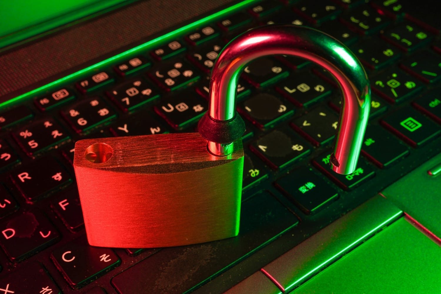 An open padlock resting on a laptop keyboard bathed in red and green light, symbolizing a cybersecurity breach