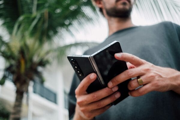 Man holding a foldable smartphone partially open, showing the rear camera array and folding hinge