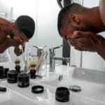 Man washing his face at a bathroom sink lined with Lumin skincare products including Moisturizing Balm and Dark Circle Defense