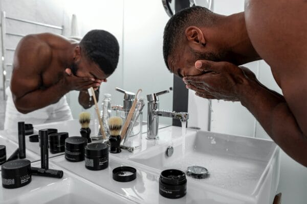 Man washing his face at a bathroom sink lined with Lumin skincare products including Moisturizing Balm and Dark Circle Defense