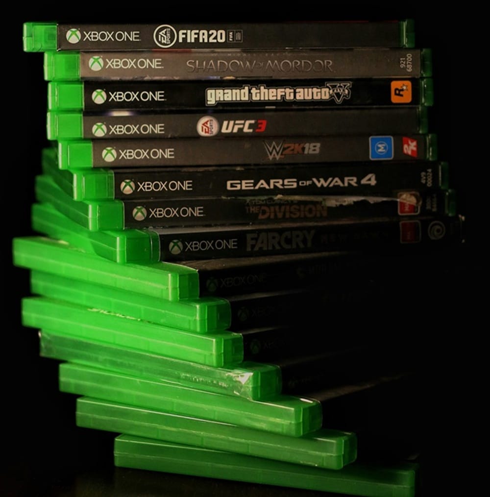Stack of Xbox One physical game disc cases including FIFA 20, Shadow of Mordor, GTA V, UFC 3, W2K18, Gears of War 4, The Division, and Far Cry